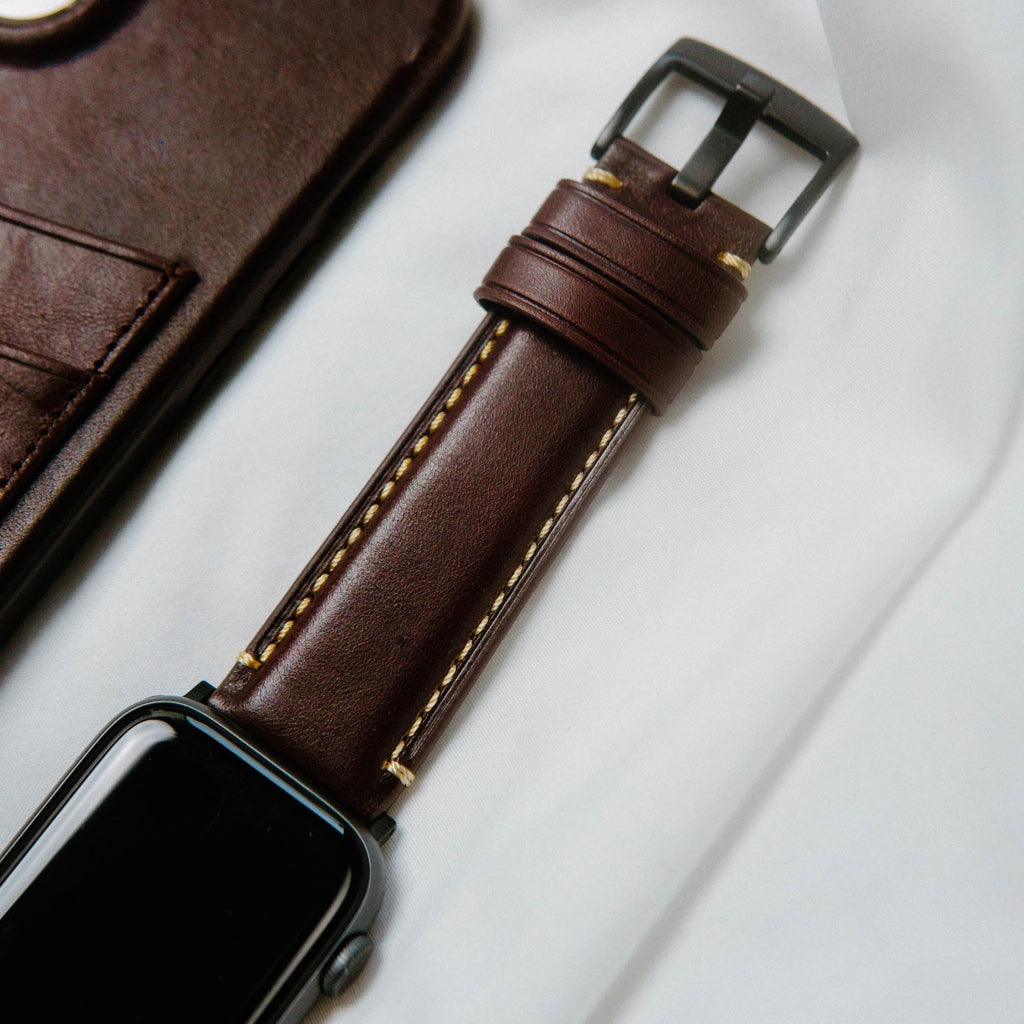 Close-up of a brown leather Apple Watch strap with yellow stitching on a white surface