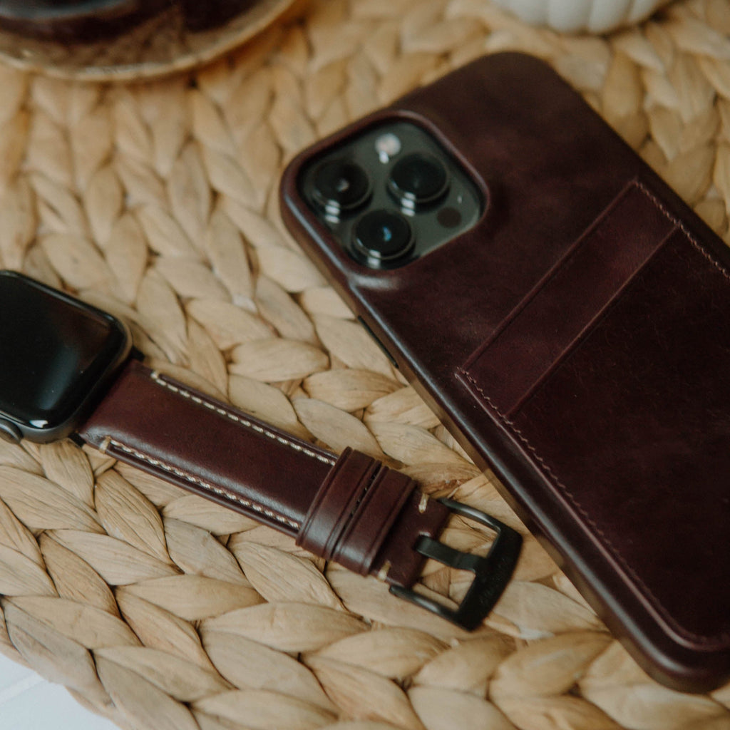 Brown leather Apple Watch strap next to a phone on a woven surface