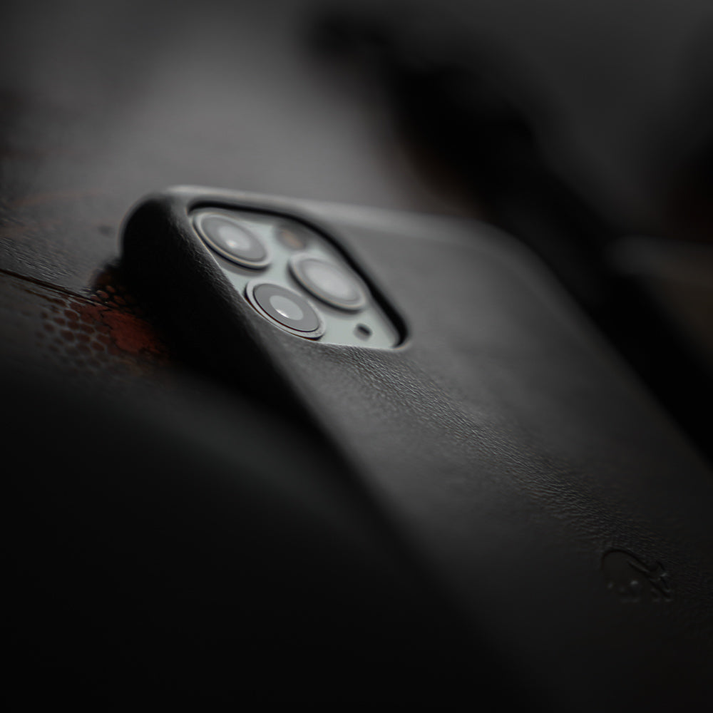 Close-up of a smartphone's triple rear camera in a black leather case on a dark textured surface.