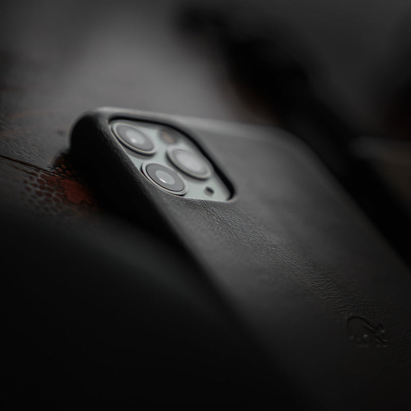 Close-up of a smartphone's triple rear camera in a black leather case on a dark textured surface.