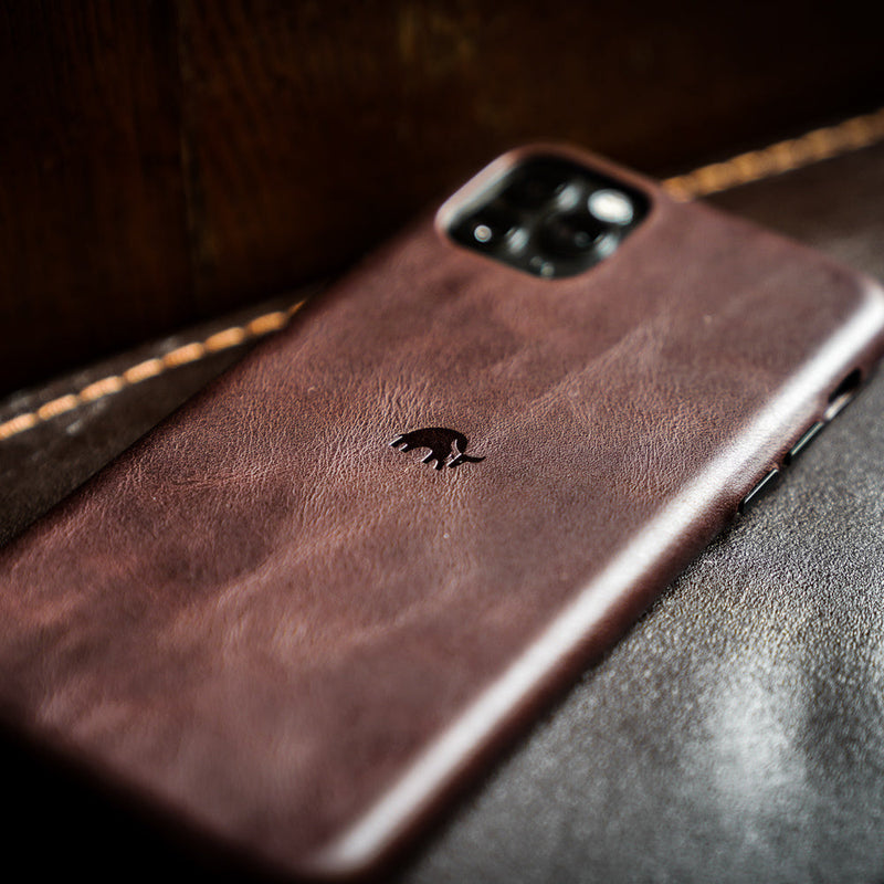 Brown leather phone case with small embossed fox logo, close-up showing textured back and camera cutout.