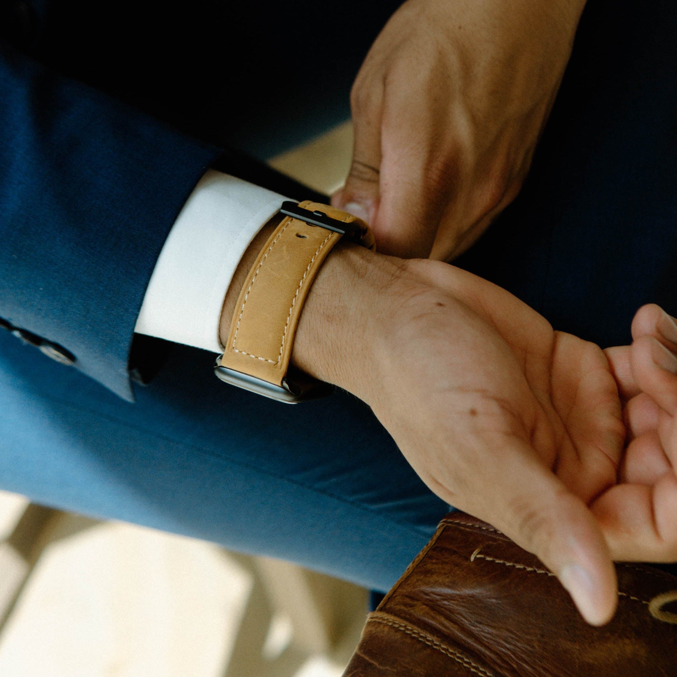 A person adjusting a leather Apple Watch strap on their wrist, showcasing the strap's color and design.