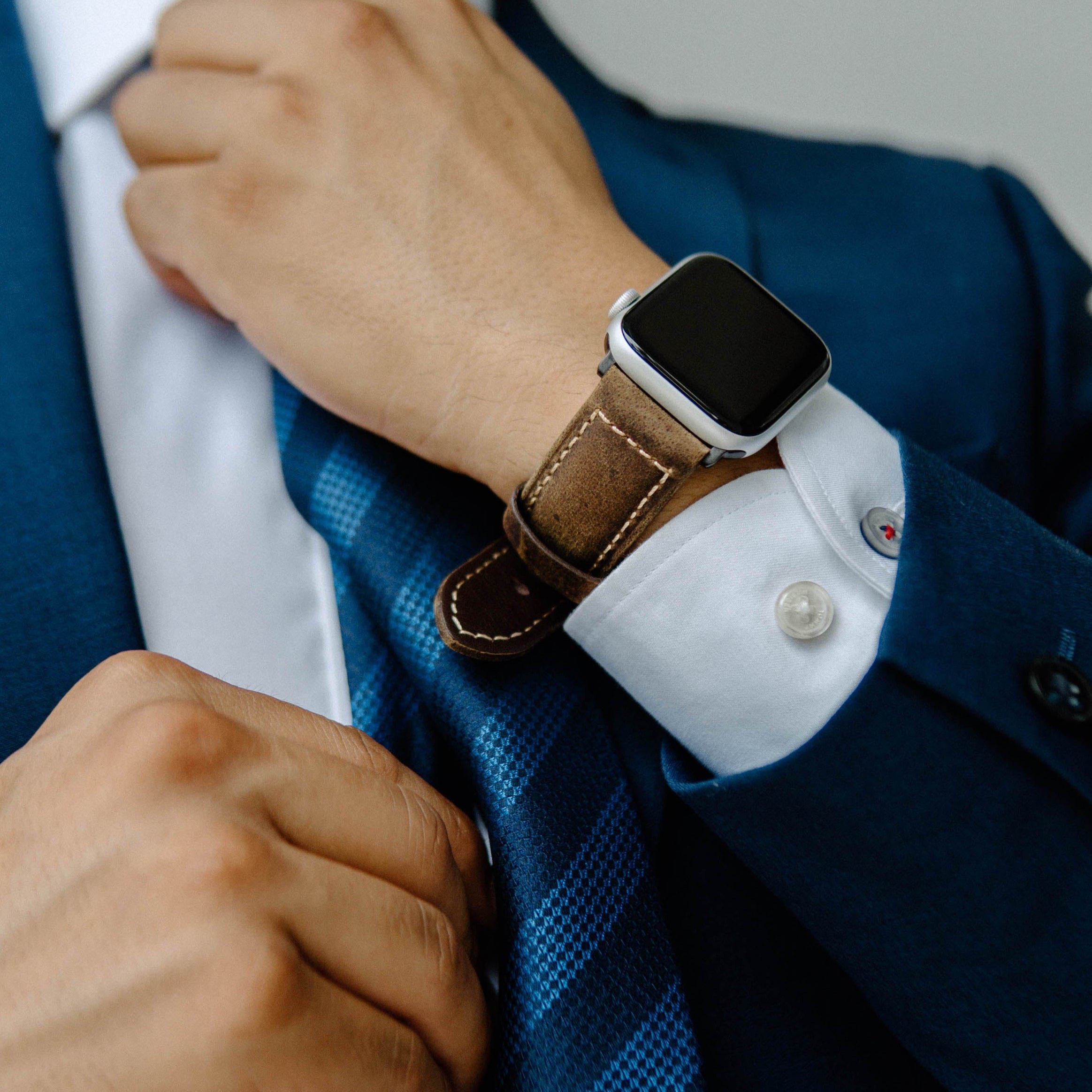 A person adjusting their suit while wearing a brown leather Apple Watch strap.