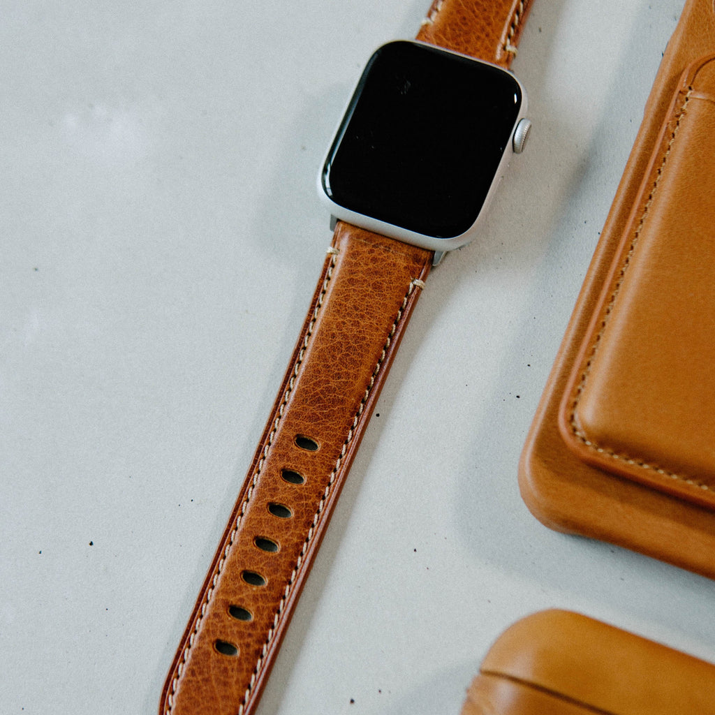 Brown leather Apple Watch strap on a light surface with accessories