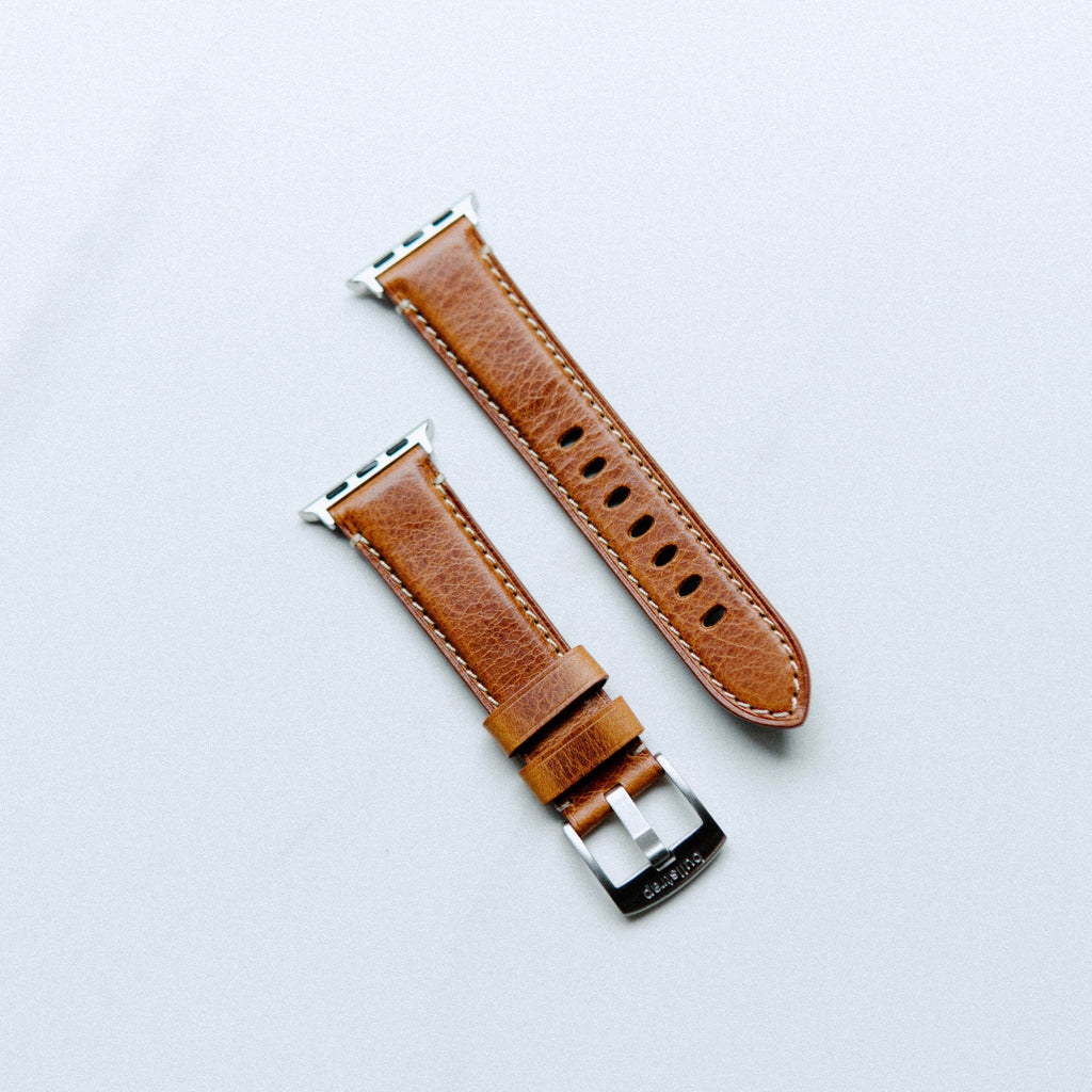 Brown leather Apple Watch strap with silver hardware, showing two pieces.