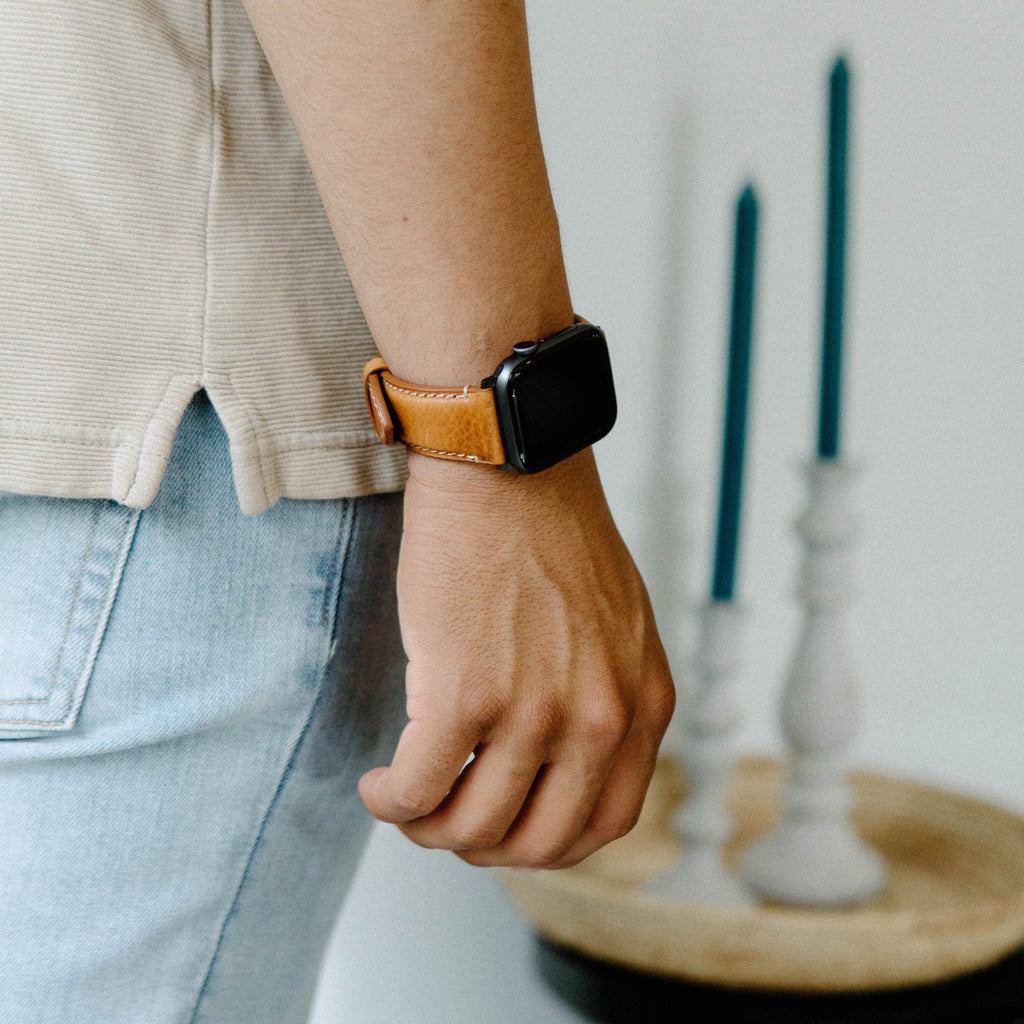 A person wearing a leather Apple Watch strap in Sienna color, with a blurred background of candles.