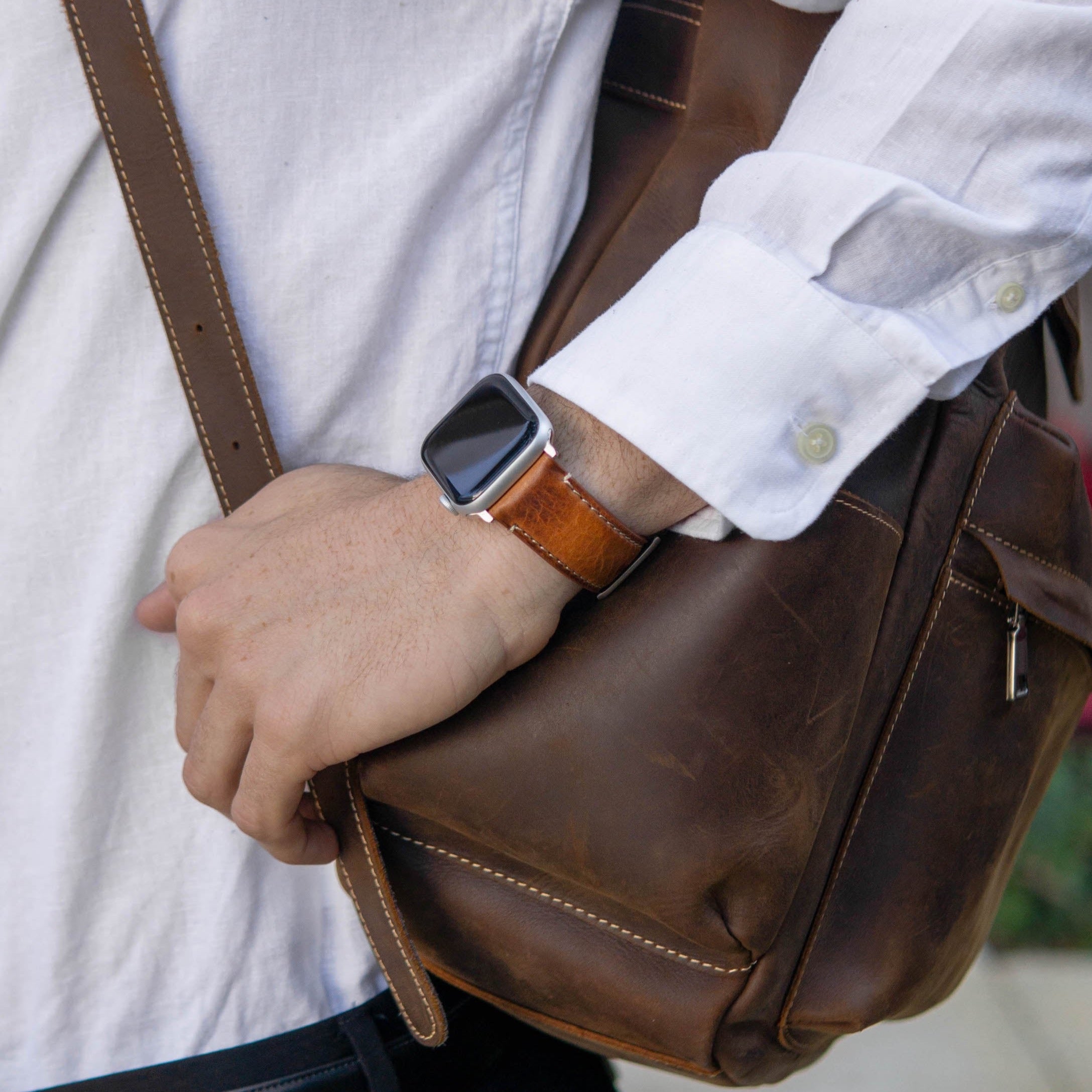 A person wearing a leather Apple Watch strap while holding a brown leather bag.