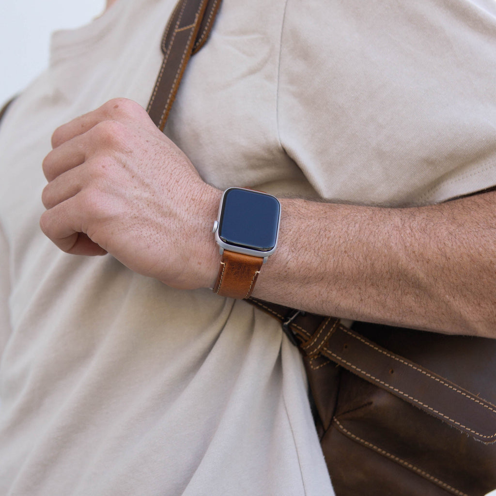 A person wearing a brown leather Apple Watch strap on their wrist, holding a bag.