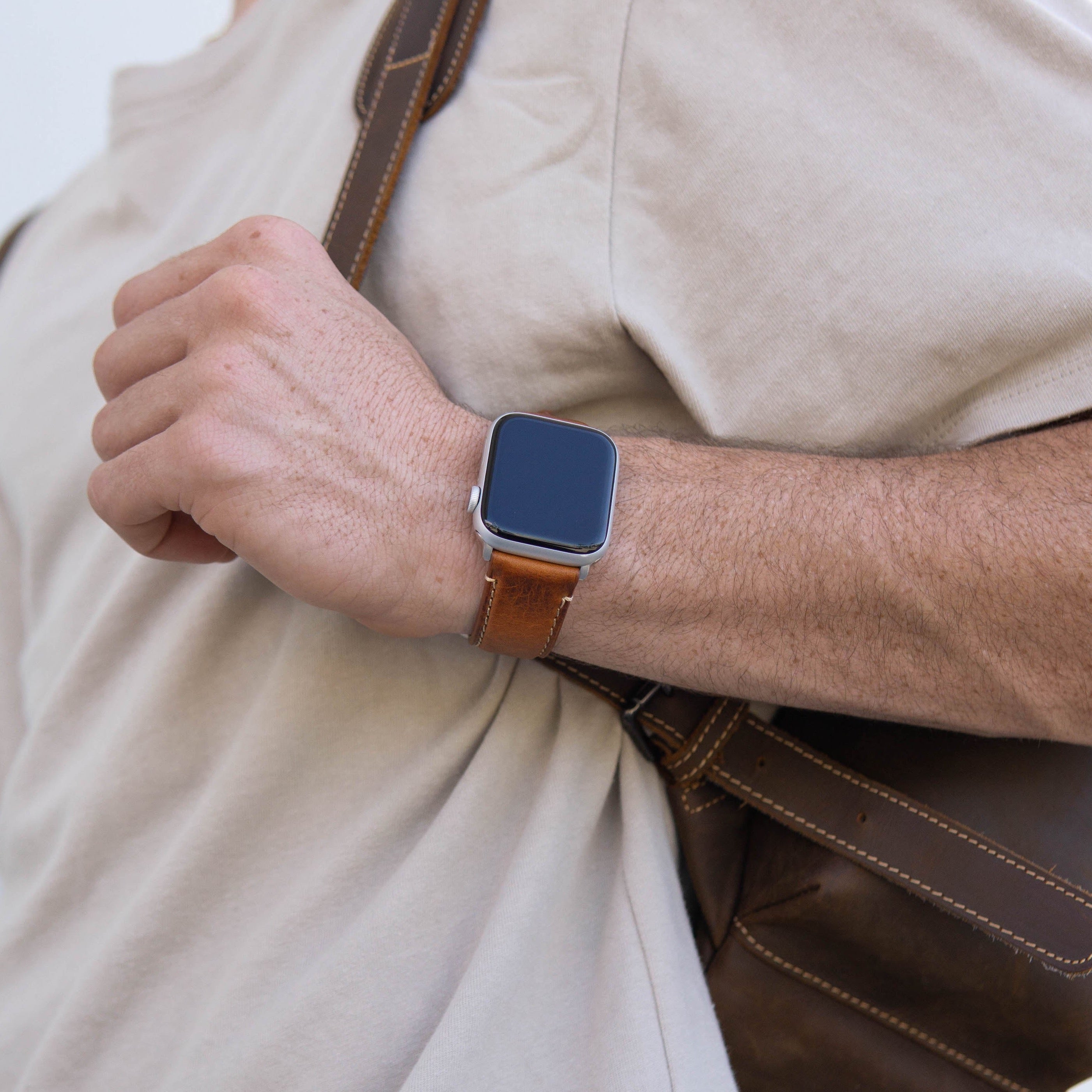 A person wearing a brown leather Apple Watch strap on their wrist, holding a bag.