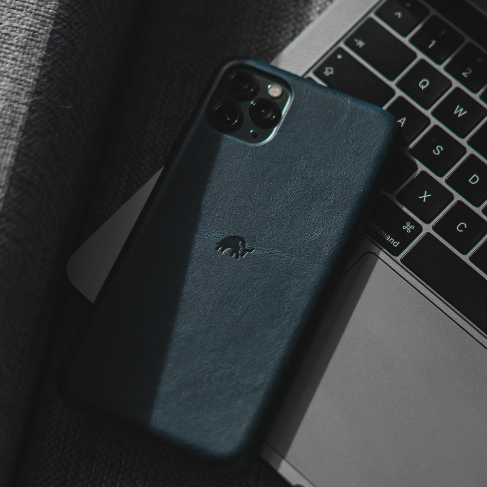 Navy leather iPhone case with embossed elephant resting on a laptop keyboard; visible keys: command A S D W X C