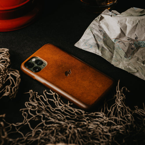 Brown leather iPhone case on a textured surface with a crumpled map nearby.