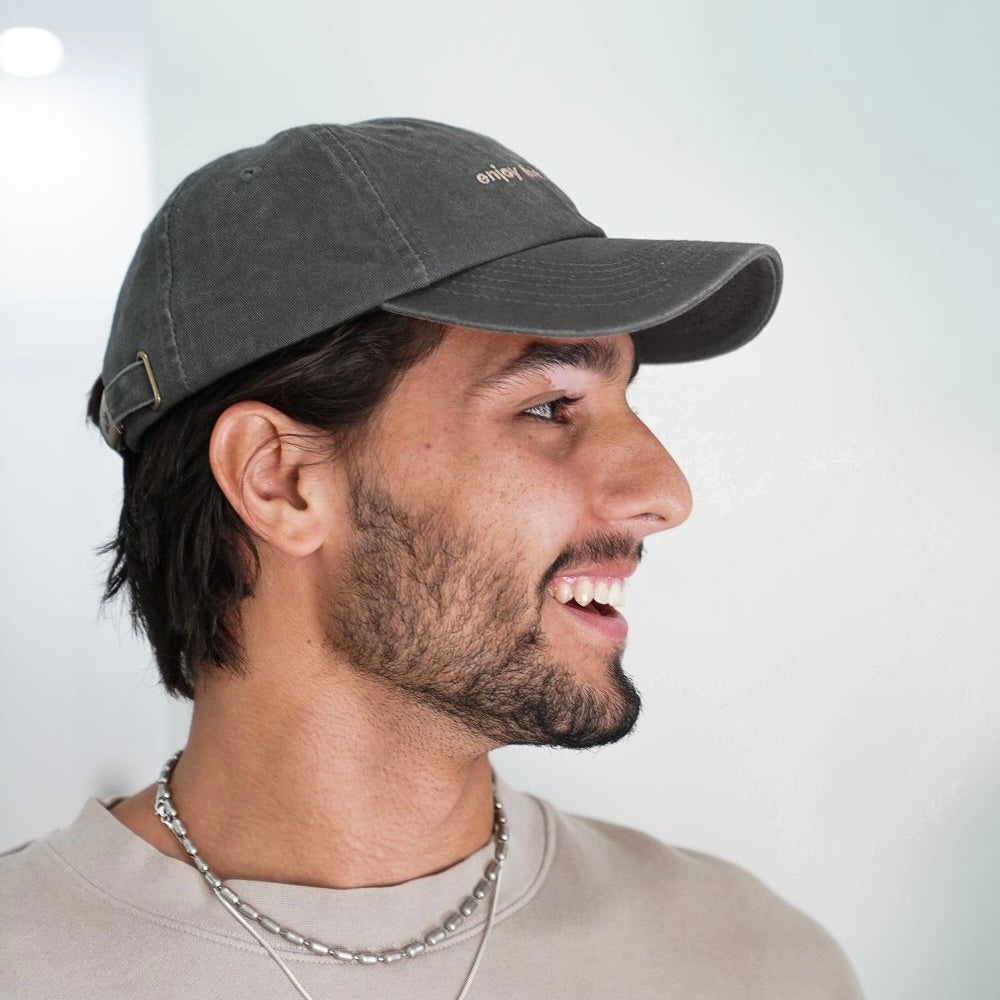 Profile view of a man wearing a grey Journey Dad Hat with 'enjoy the journey' embroidered on it.