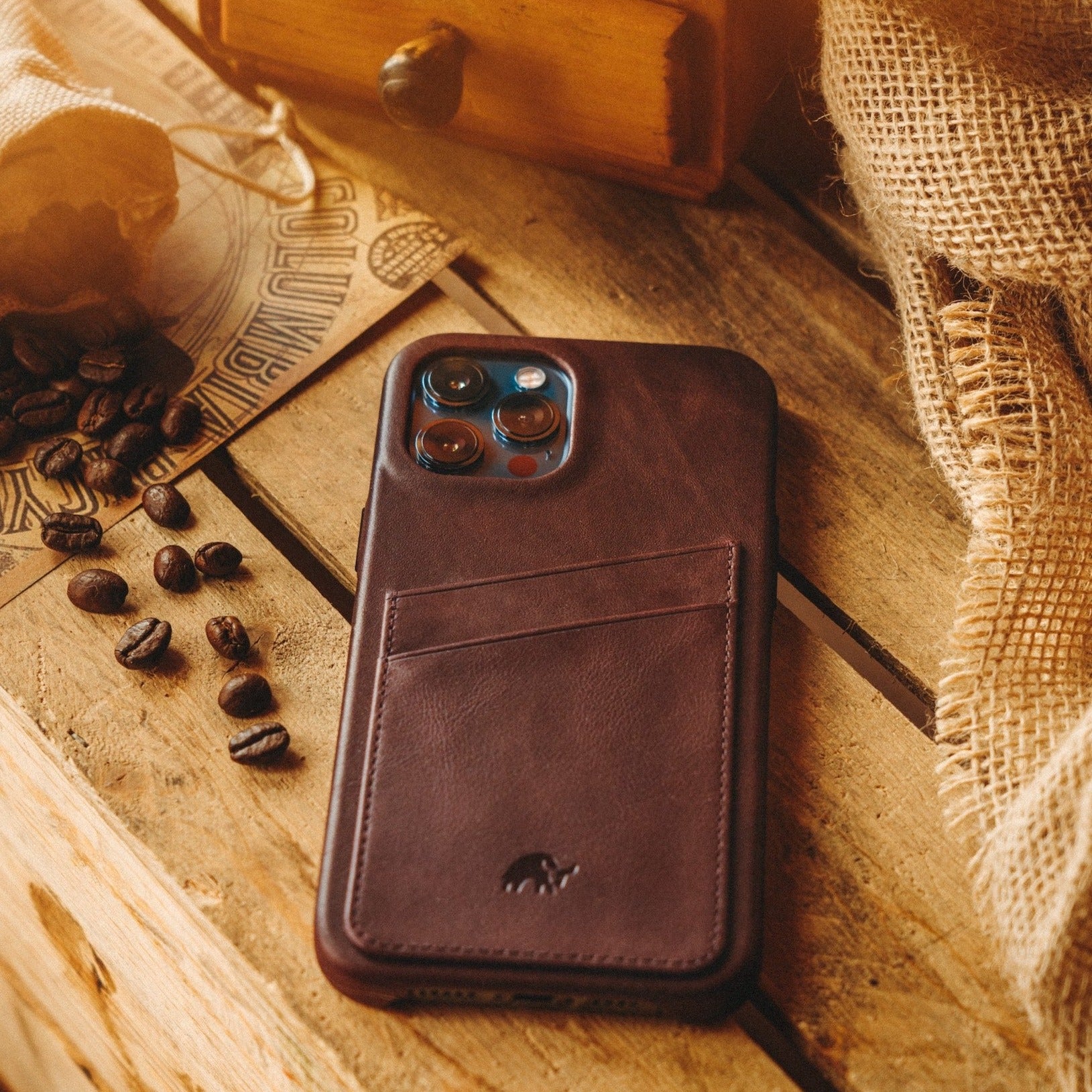 Brown leather iPhone case with card slot on back, placed on wooden surface with coffee beans