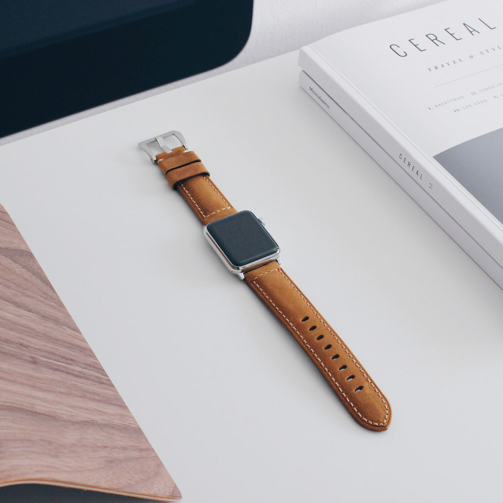 Smartwatch with brown stitched leather band on a white desk beside a CEREAL magazine — TRAVEL & STYLE