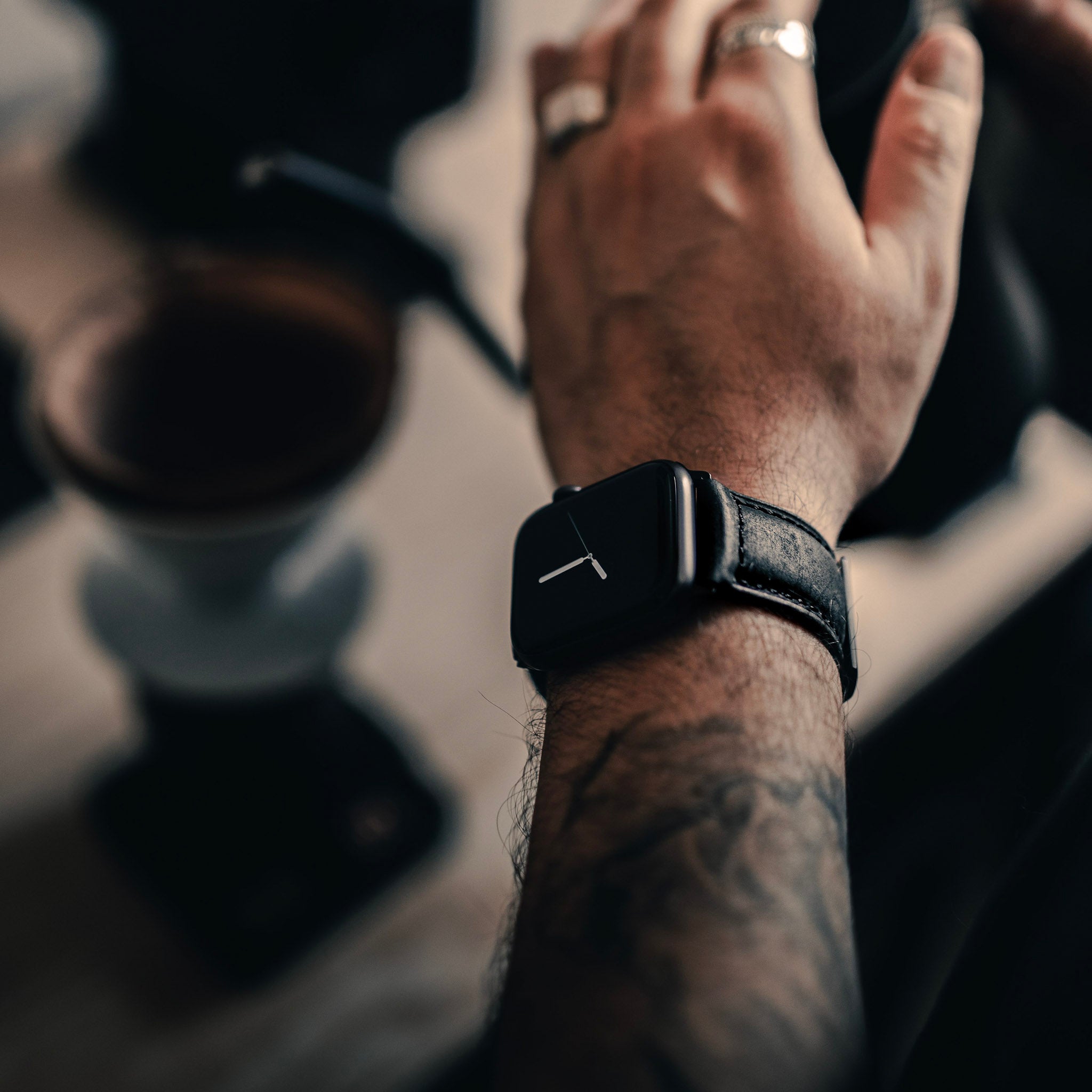 A person wearing a matte black leather Apple Watch strap on their wrist.