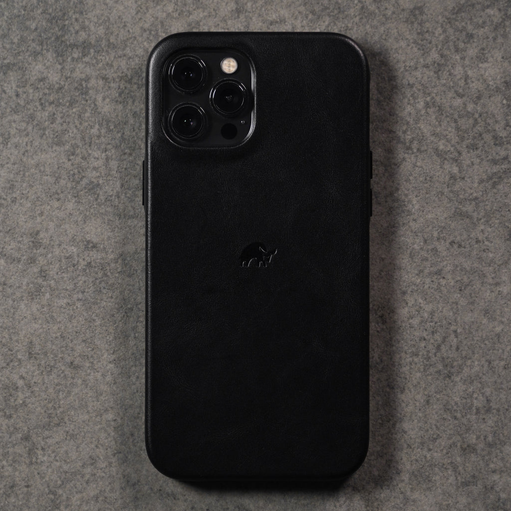 Rear view of black Classic iPhone case in leather showing embossed logo and camera cutout on textured gray background
