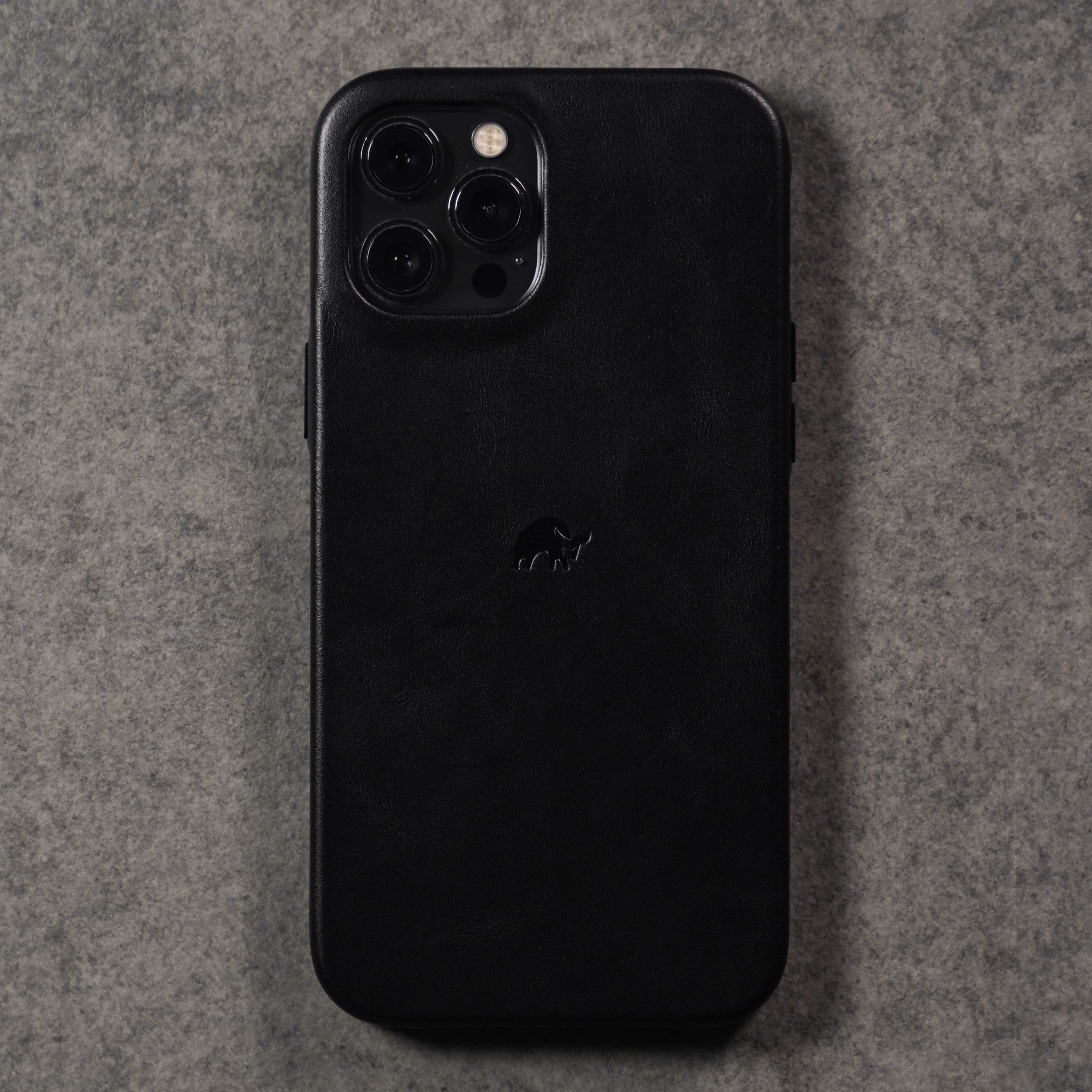 Rear view of black Classic iPhone case in leather showing embossed logo and camera cutout on textured gray background