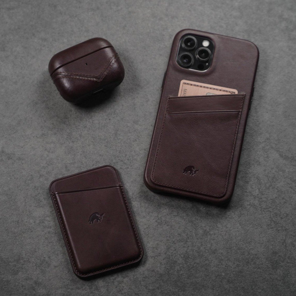Bourbon leather iPhone wallet with card in pocket, leather AirPods case, and matching leather card sleeve on gray background.