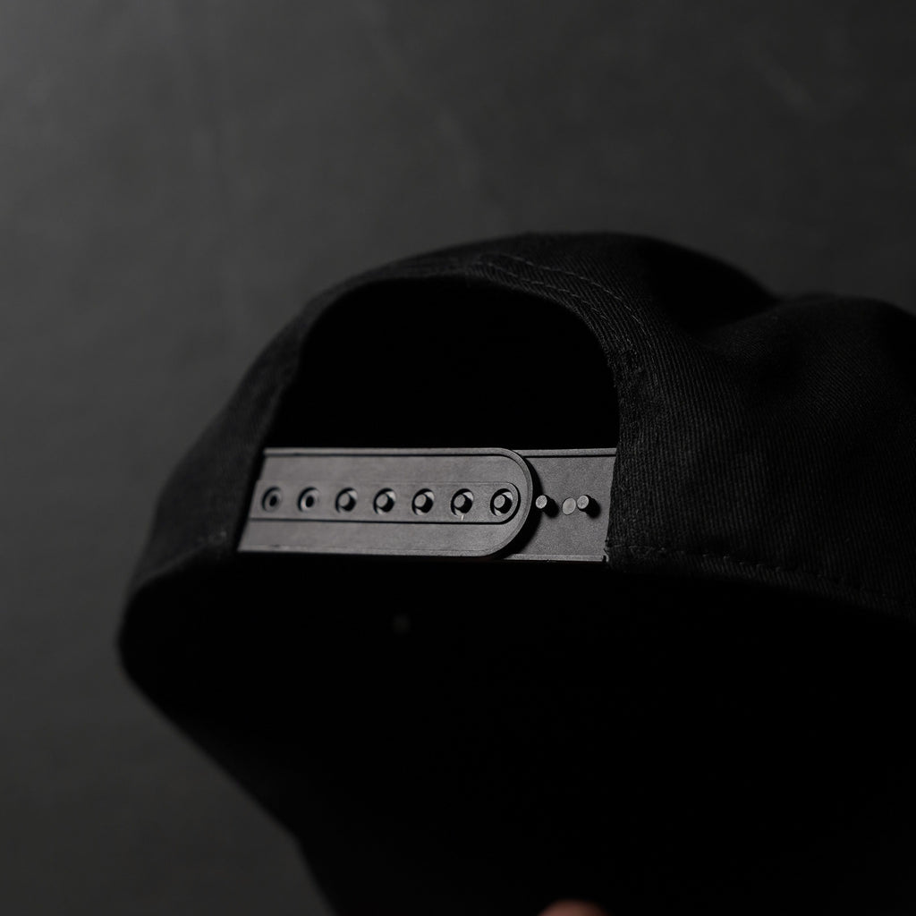 Back of a black snapback hat showing adjustable plastic snap strap