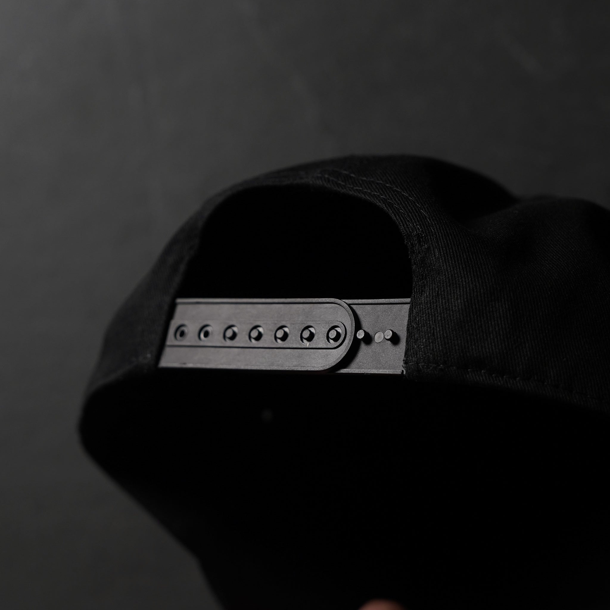 Back of a black snapback hat showing adjustable plastic snap strap