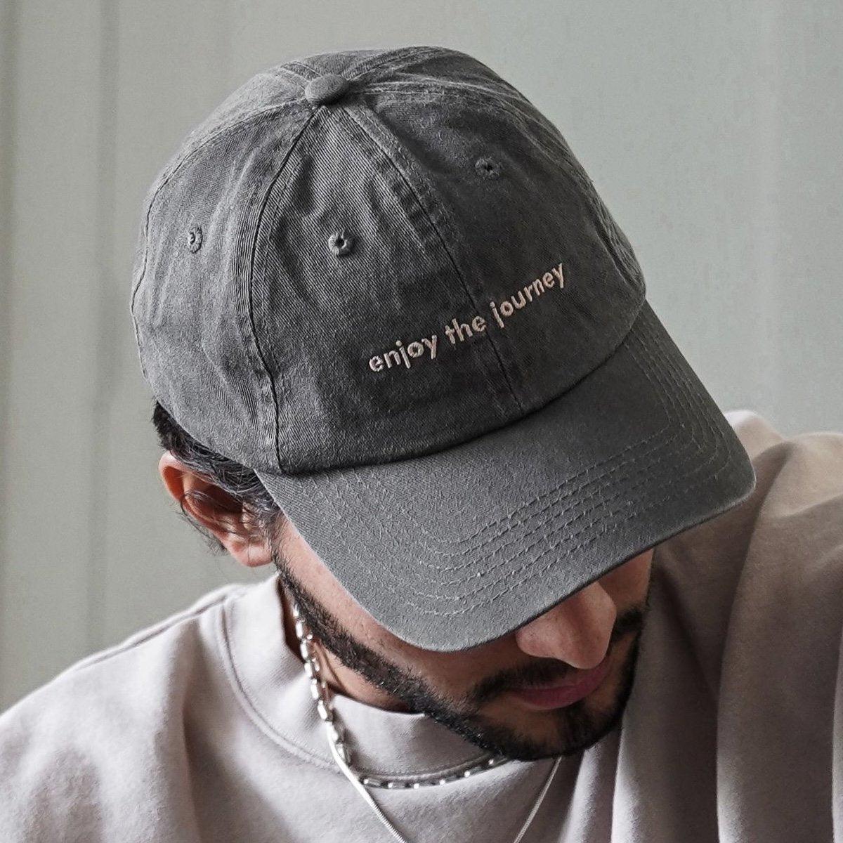 A grey Journey Dad Hat with the text 'enjoy the journey' embroidered on it.