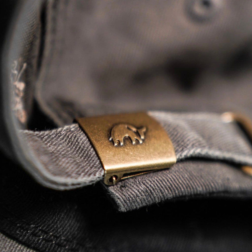 Close-up of the brass buckle on the Journey Dad Hat, featuring a bull logo