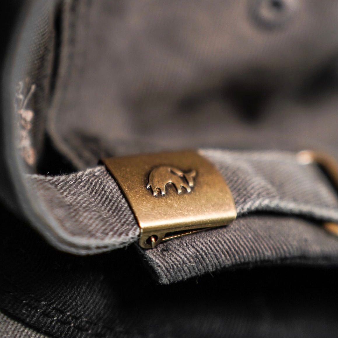 Close-up of the brass buckle on the Journey Dad Hat, featuring a bull logo
