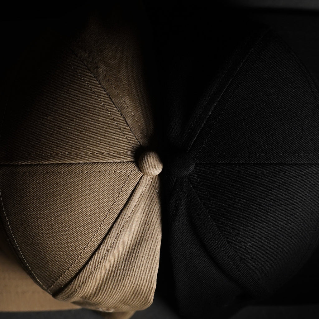 Top view of the EYJ Badge Hat in tan and black, showing the texture and button detail.
