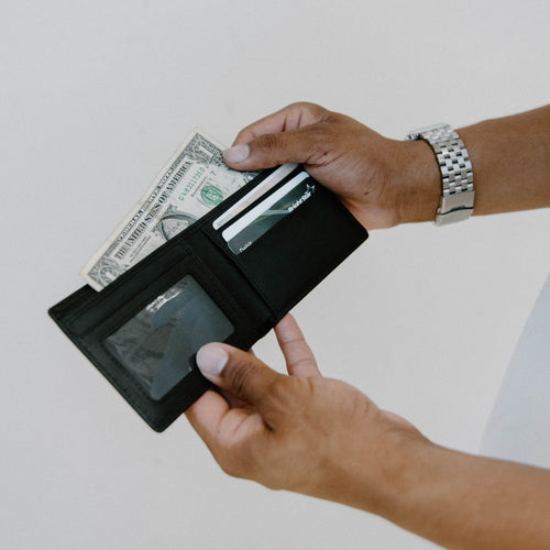 A person holding a bifold wallet open, showing cash and cards inside.