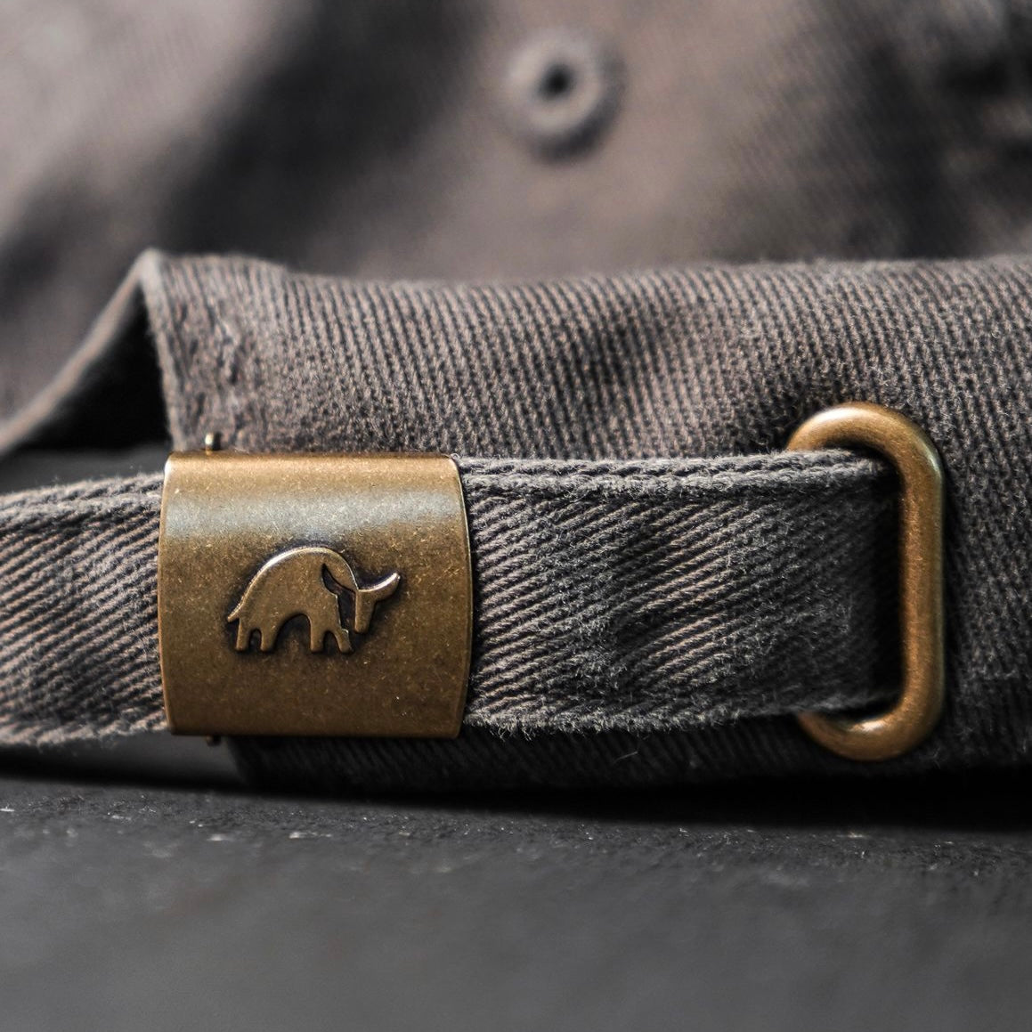 Close-up of the adjustable strap and brass hardware of the Journey Dad Hat in grey.