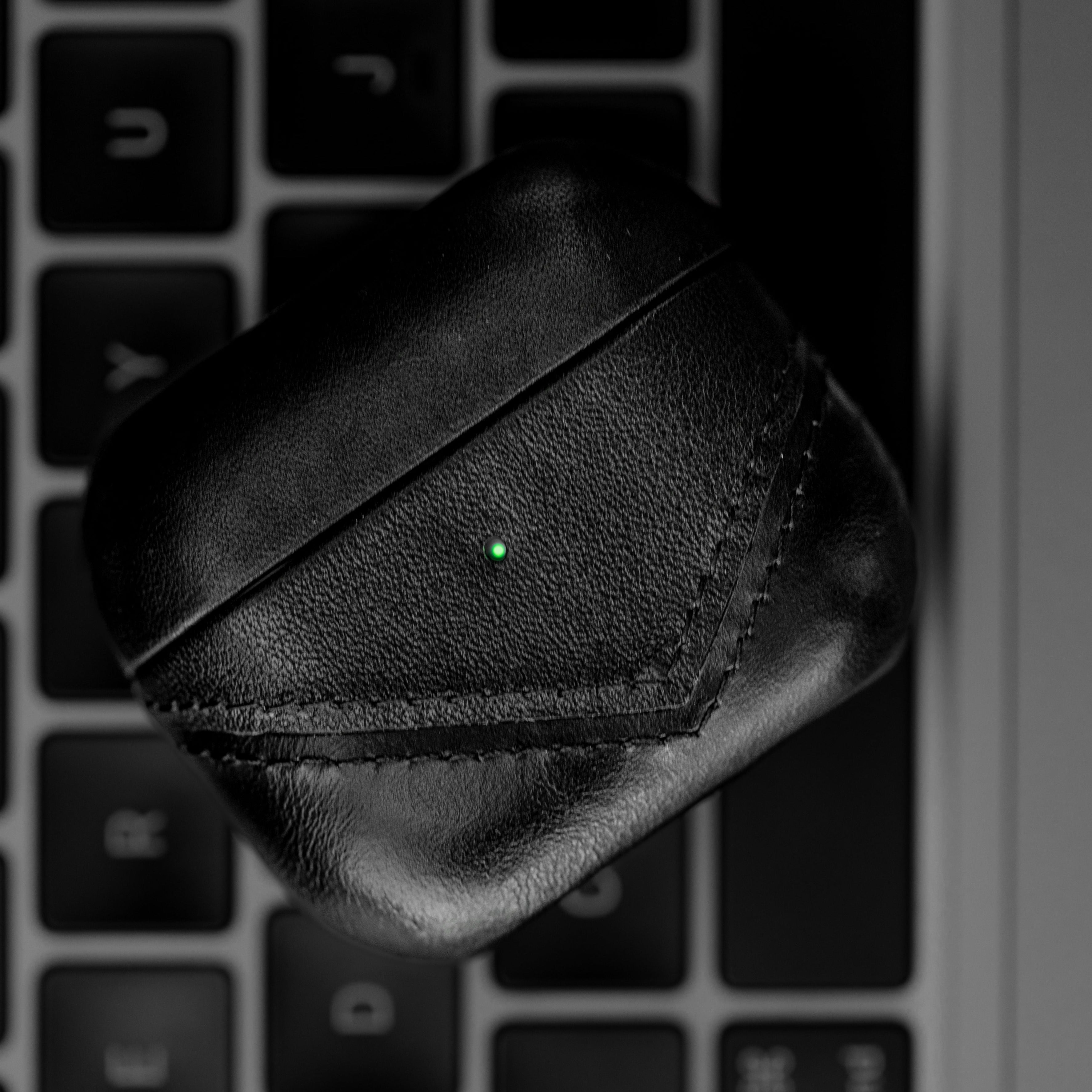 Black leather AirPods case on a keyboard with a green indicator light