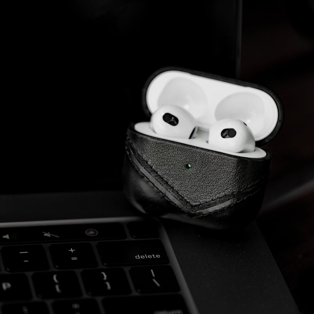 Black leather AirPods case with AirPods inside, placed on a laptop keyboard