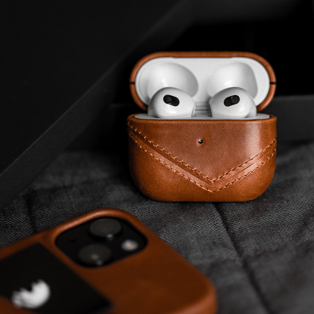 Brown leather AirPods case with AirPods inside, showcasing stitching detail.