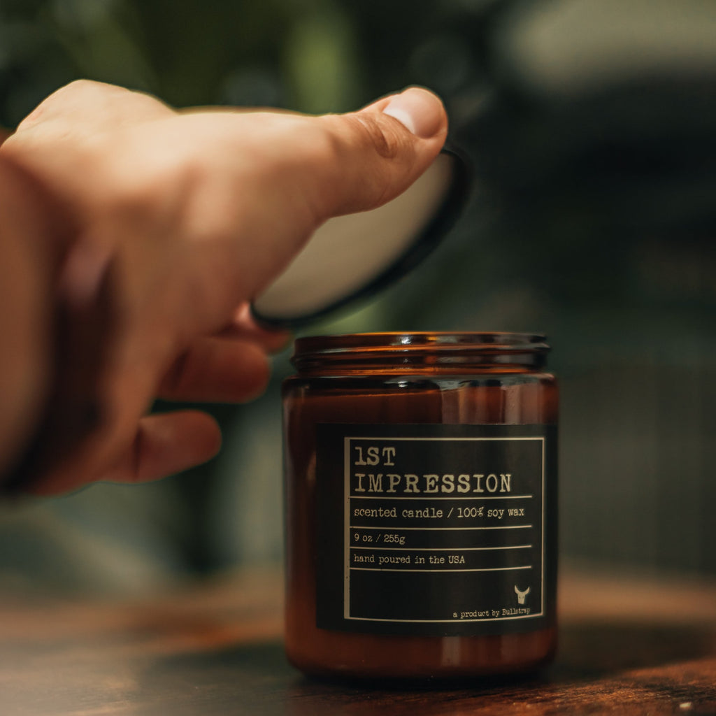 A hand opening a jar of 1st Impression Candle, 9 oz, scented candle made of 100% soy wax, hand poured in the USA.