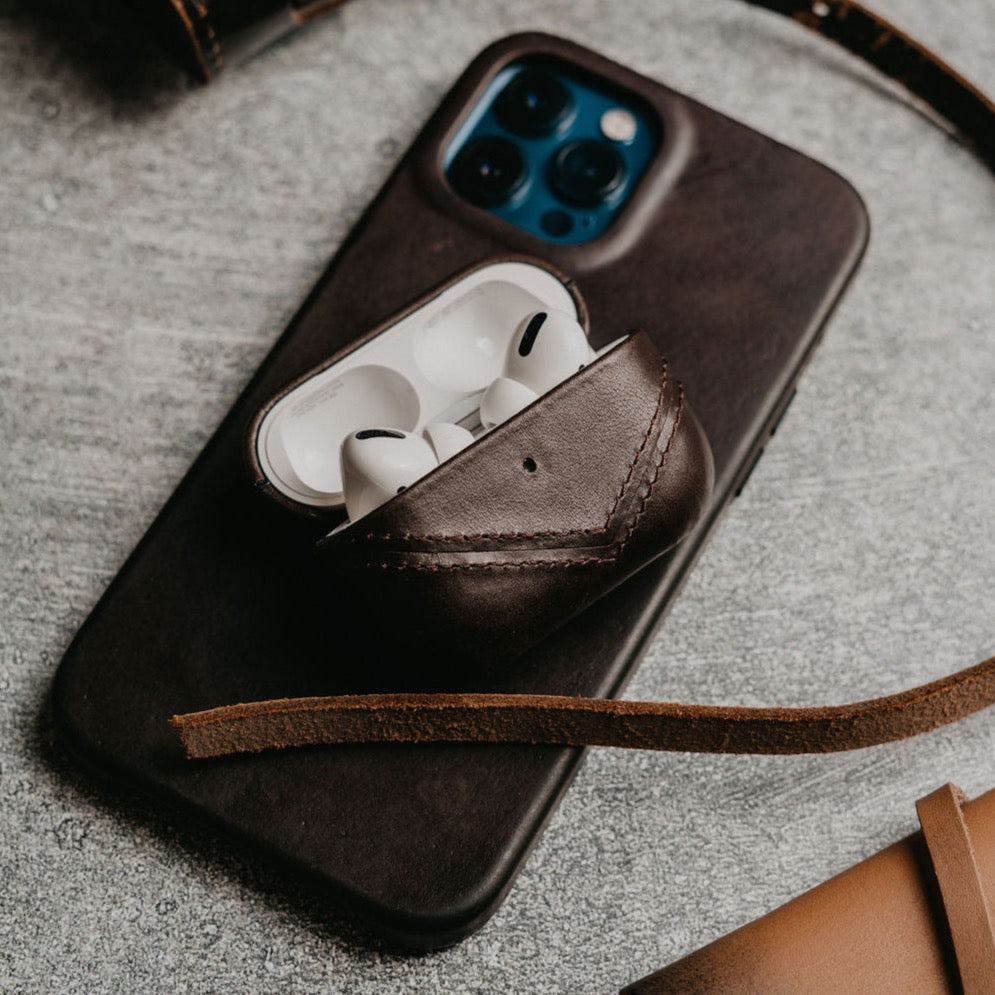 Brown leather AirPods case with AirPods inside on a dark surface