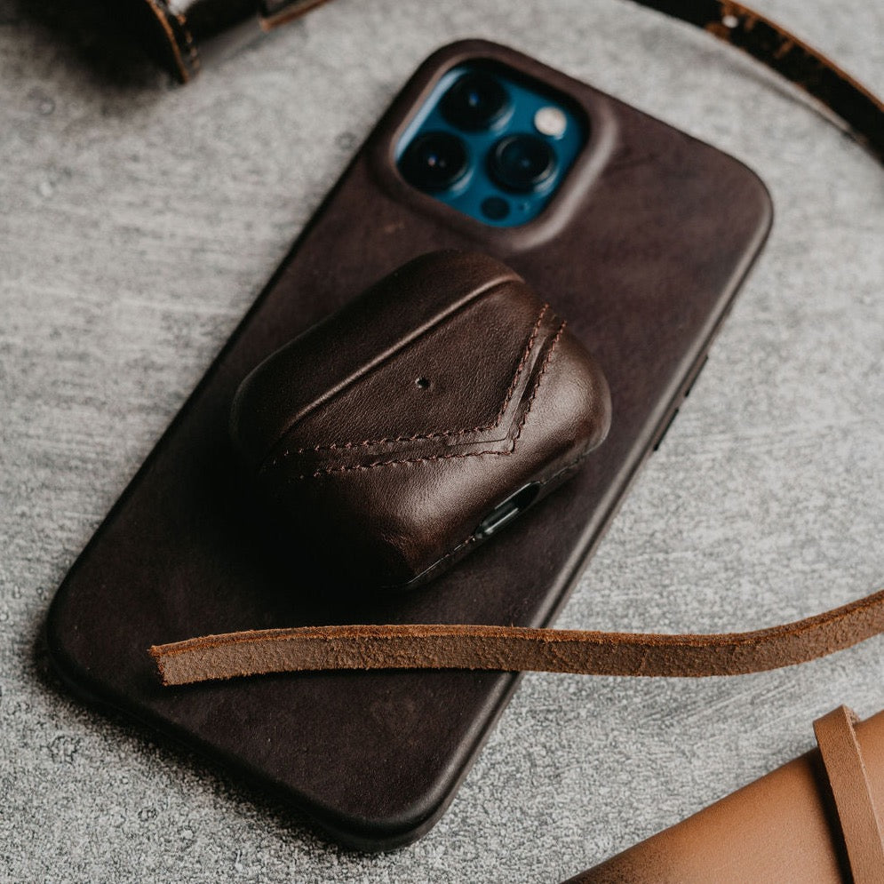 Brown leather iPhone case with AirPods case on top, on a dark surface