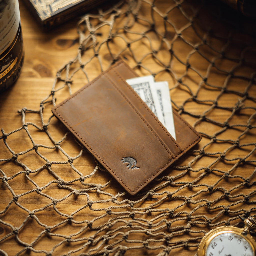 Brown leather card holder with cash and cards visible, embossed logo.