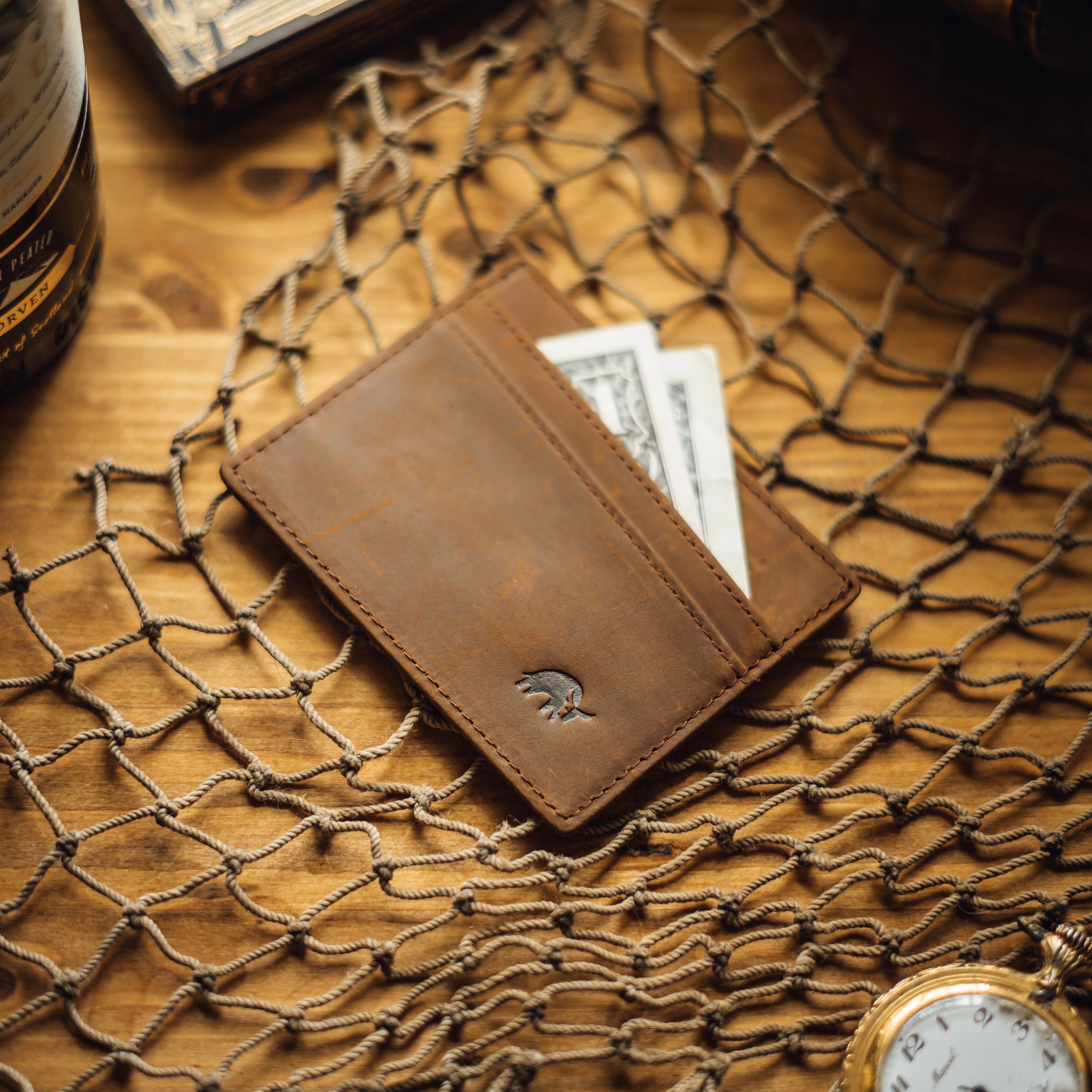 Brown leather card holder with cash and cards visible, embossed logo.