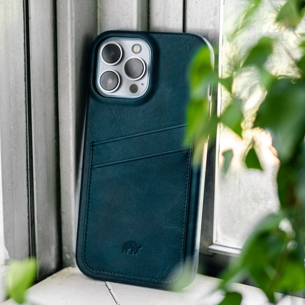 Ocean-teal leather minimalist phone case with two card slots and camera cutout leaning on a windowsill