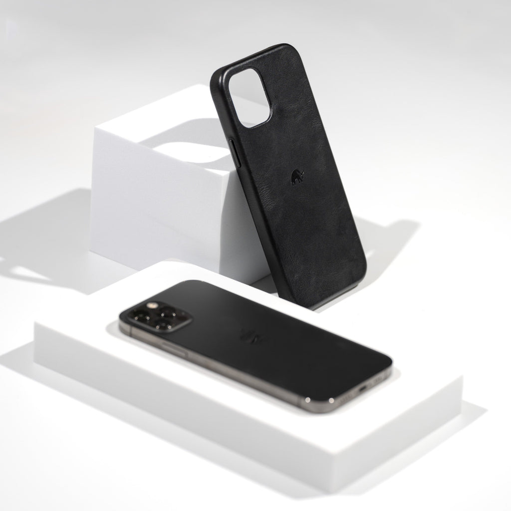 Black leather minimalist phone case standing on a white pedestal beside a black smartphone