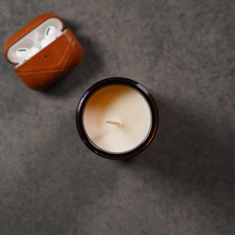 Top view of a 1st Impression Candle in a jar with a brown lid, next to a brown AirPods case.