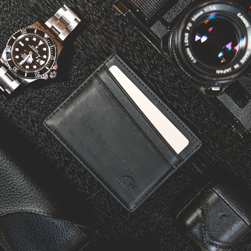 Black leather card holder with a card and a watch and camera in the background