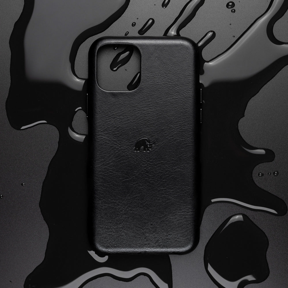 Black leather iPhone case with small embossed elephant logo, placed on wet black surface with glossy water droplets.