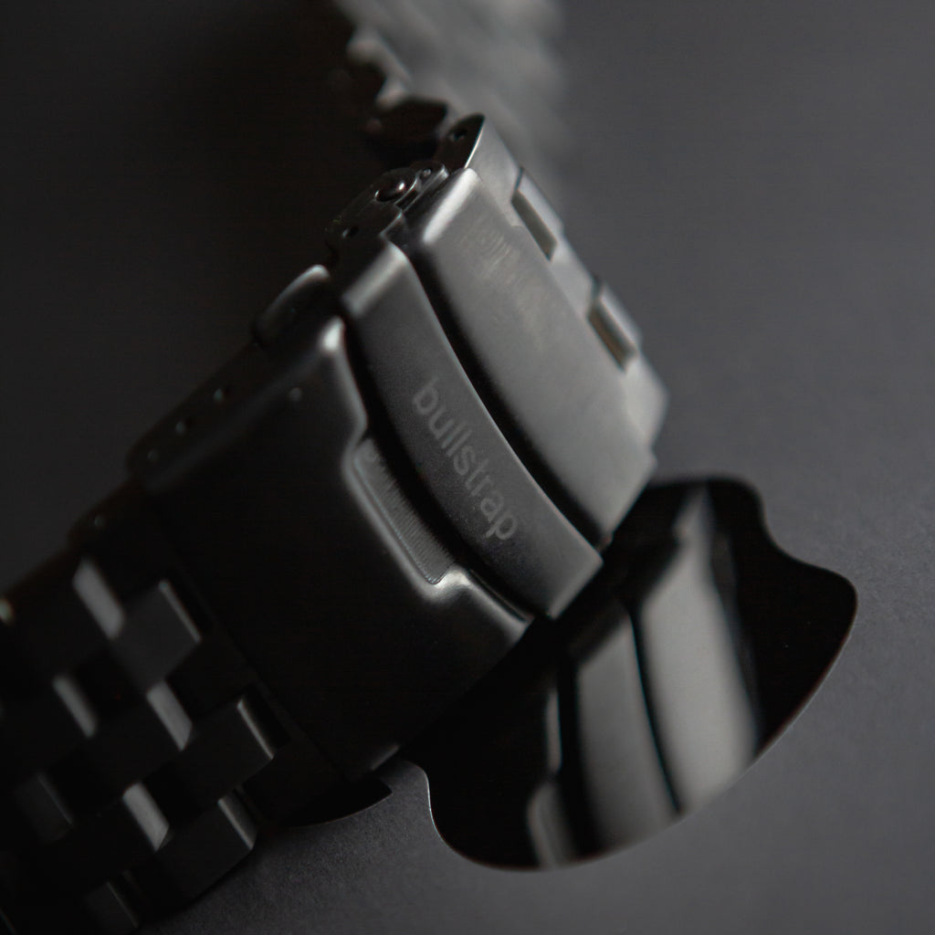 Black metal link Apple Watch strap, close-up of clasp engraved 'bullstrap'